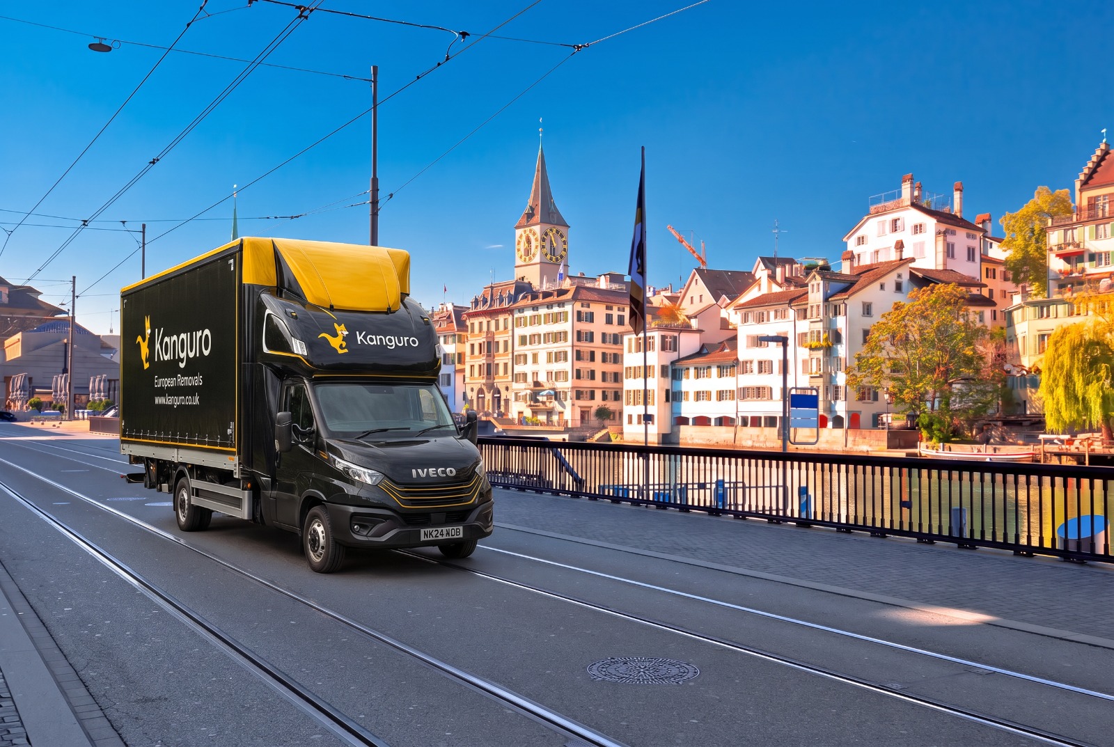 Kanguro removal van beside a river and church towers in Switzerland – shared-load removals from the UK to Switzerland