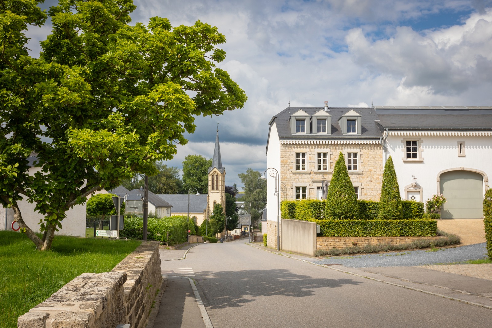 Quiet road beside a white building and stone boundary wall in Luxembourg – shared-load removals to Luxembourg